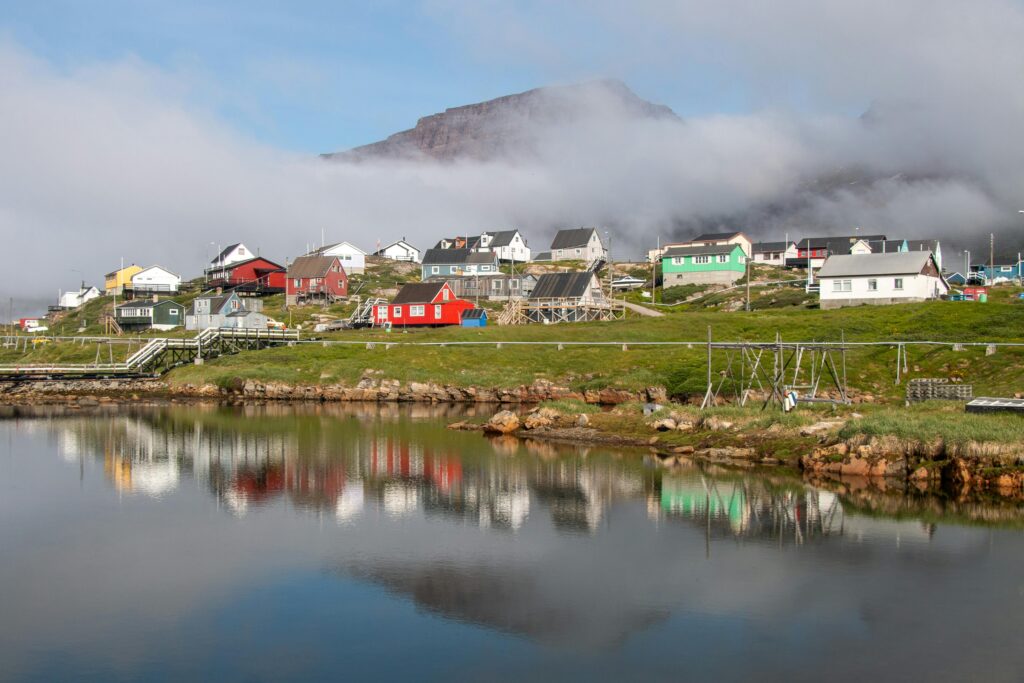 Picturesque Qeqertarsuaq village reflecting on a tranquil lake in Greenland under a cloudy sky.