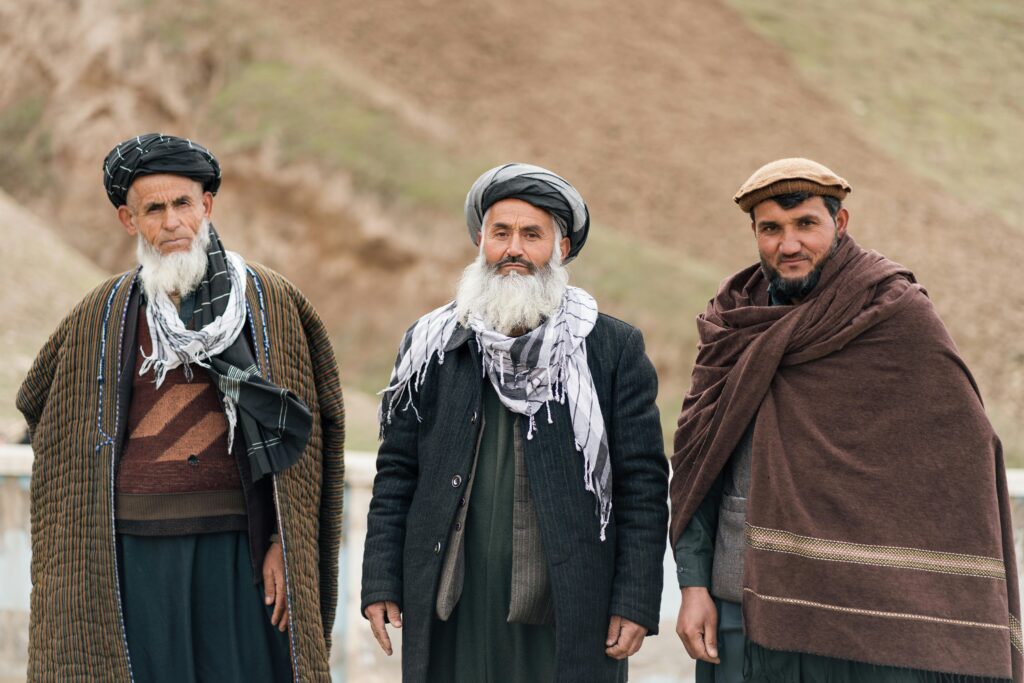 Three Afghan men in traditional attire standing outdoors, showcasing cultural attire and identity.