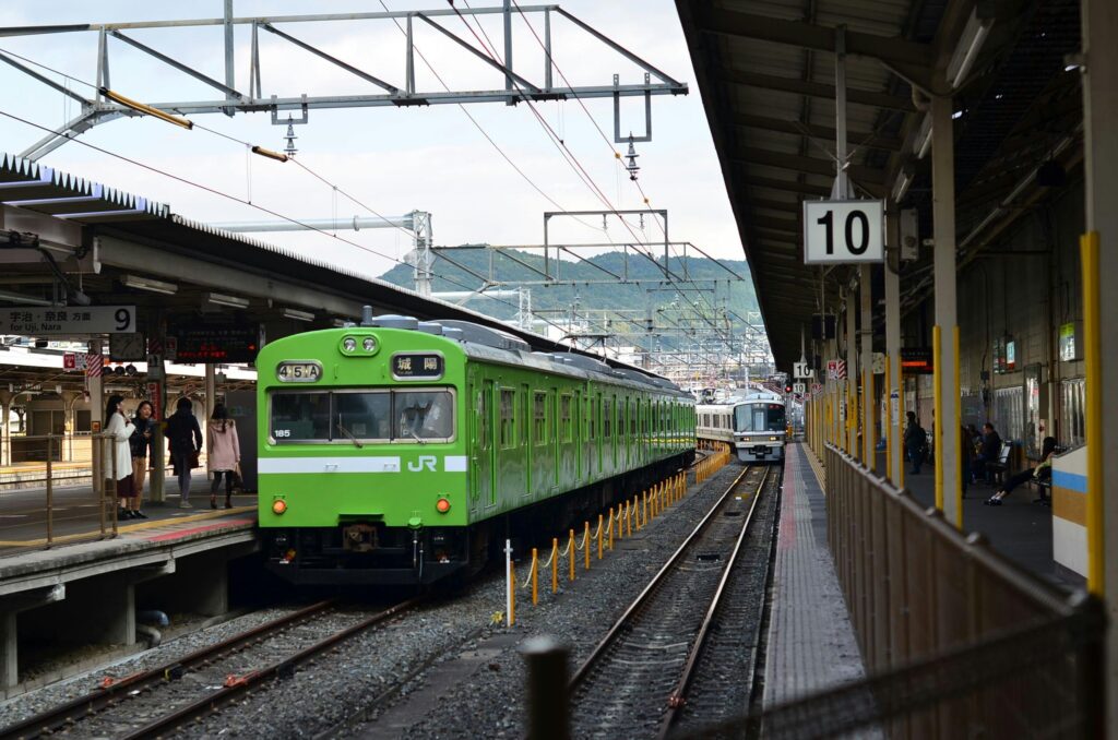 Green JR train at Kyoto station platform with passengers and distant mountains.