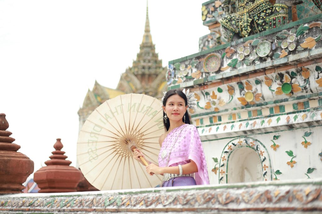 A woman in traditional Thai dress poses with a parasol at Wat Arun temple in Bangkok, Thailand.
