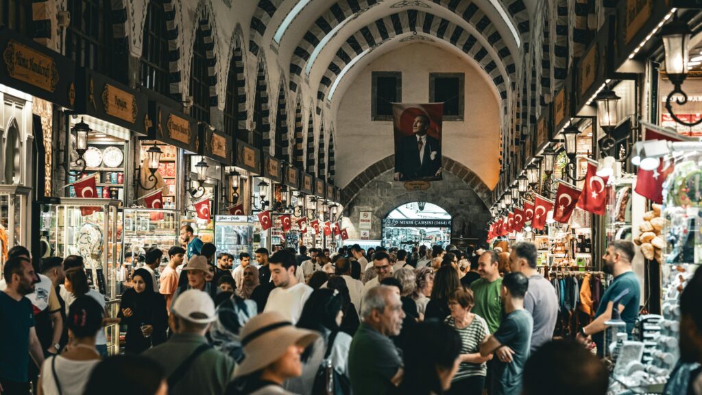 Bustling scene at Istanbul's Grand Bazaar with visitors and Turkish flags.