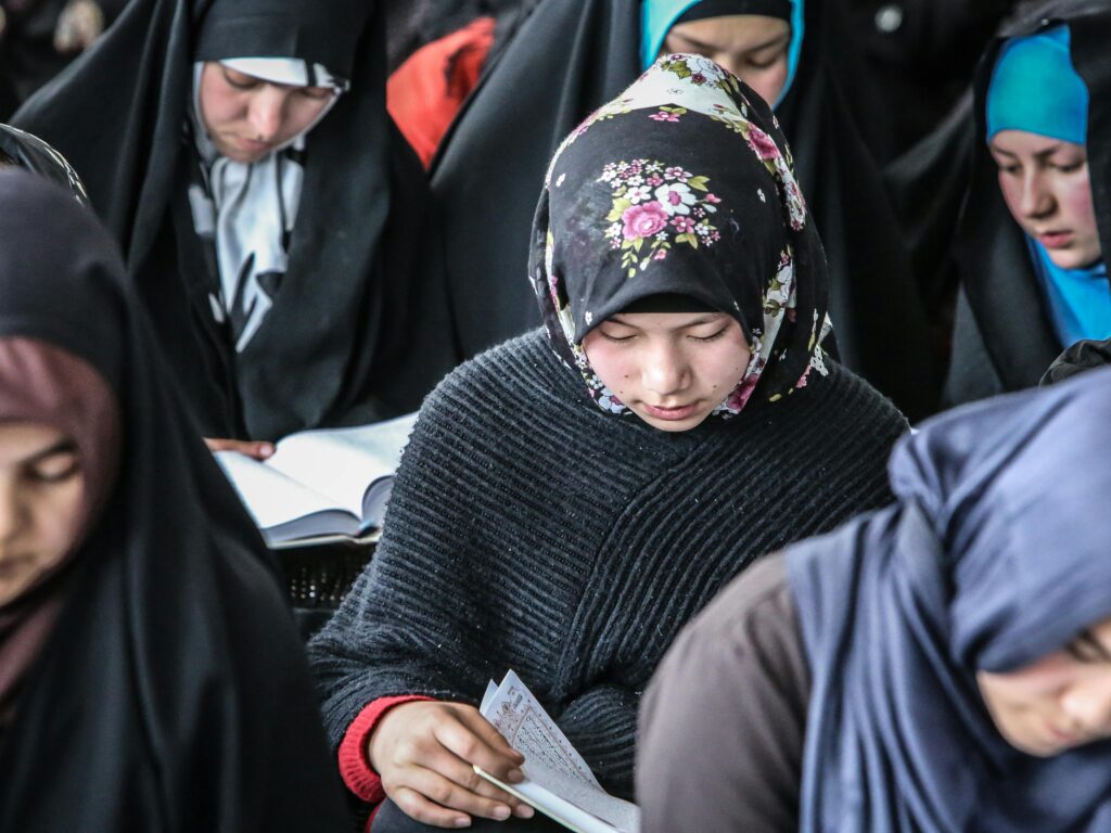 Group of Afghan girls in traditional attire focused on reading during a community event.