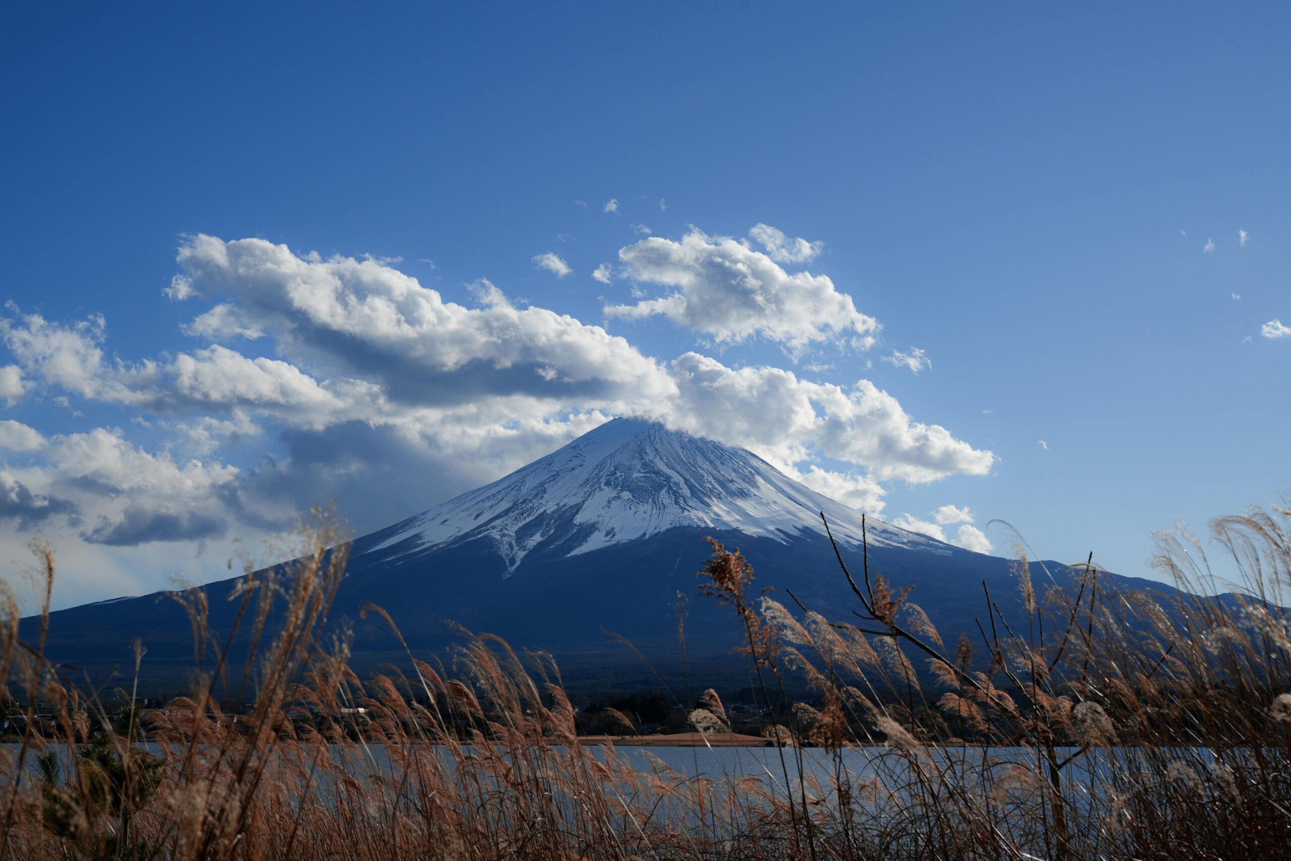 Mount Fuji with vibrant sky and clouds, seen from lake in Japan.