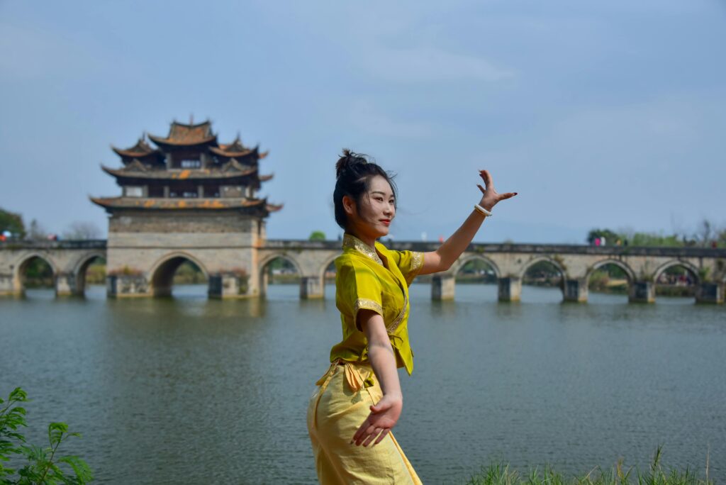 Woman dances in traditional attire by iconic ancient bridge in China.
