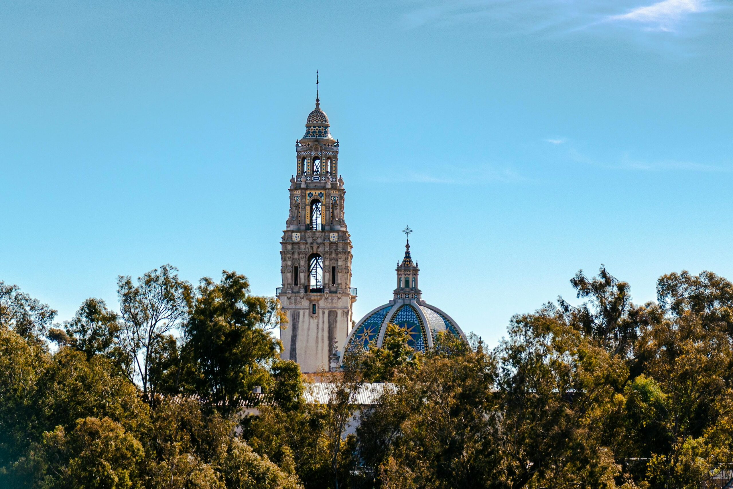 View of the California Tower at Balboa Park surrounded by trees under a clear blue sky.