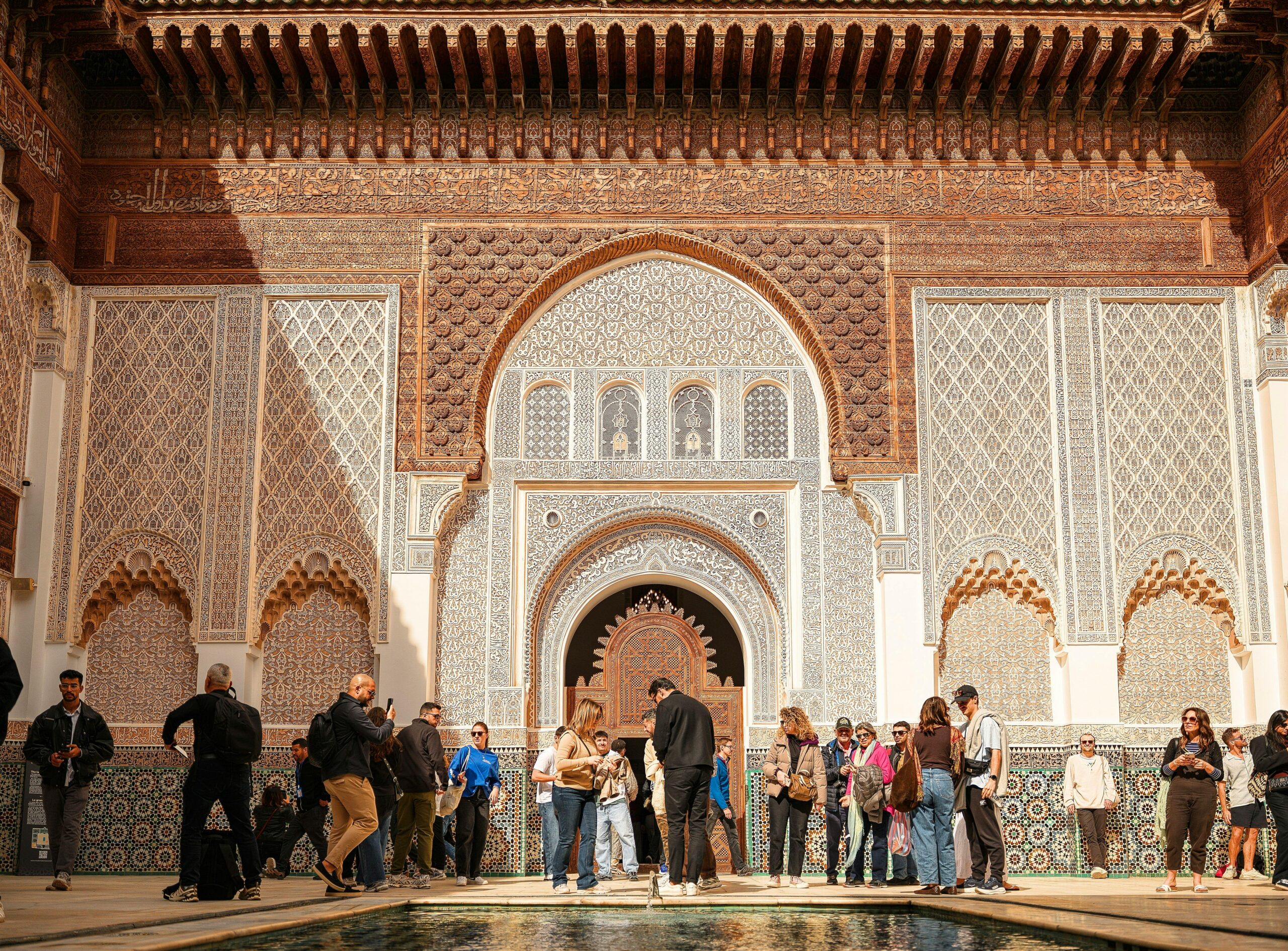 Group of tourists exploring Ben Youssef Madrasa's intricate architecture in sunny Marrakech.