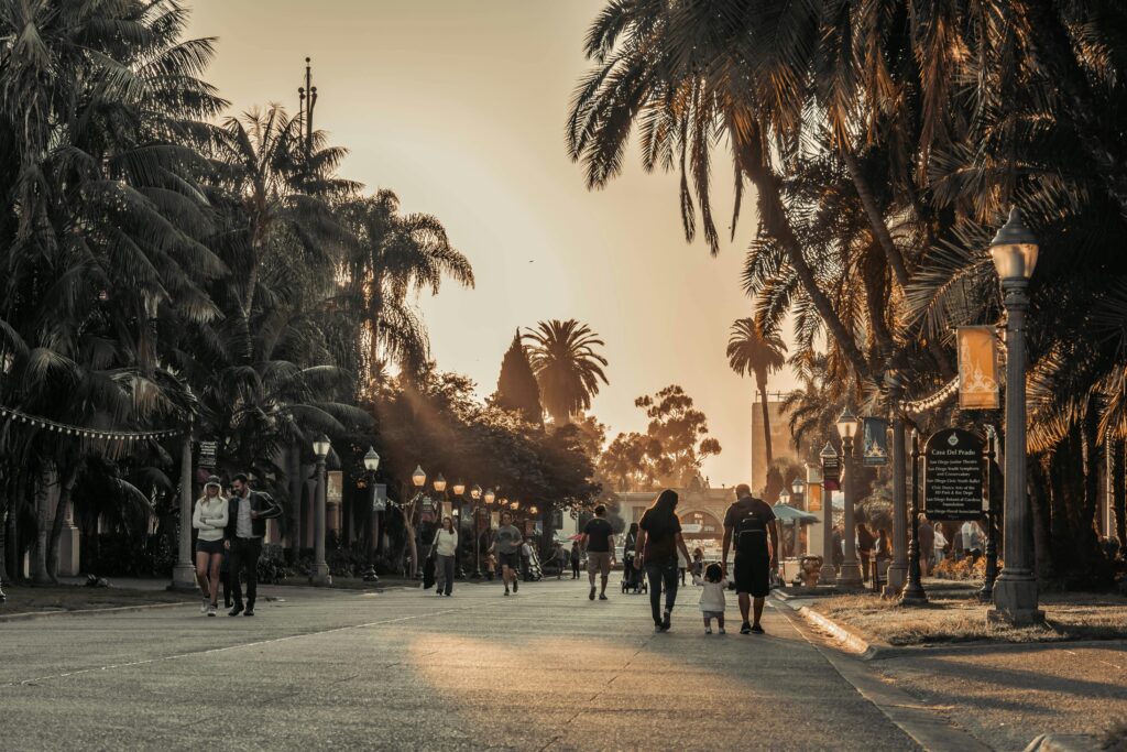 People walking under palm trees at sunset in San Diego's Balboa Park. Warm tones and relaxed atmosphere.