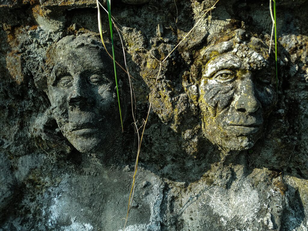 Close-up of ancient stone face sculptures embedded in a textured wall.