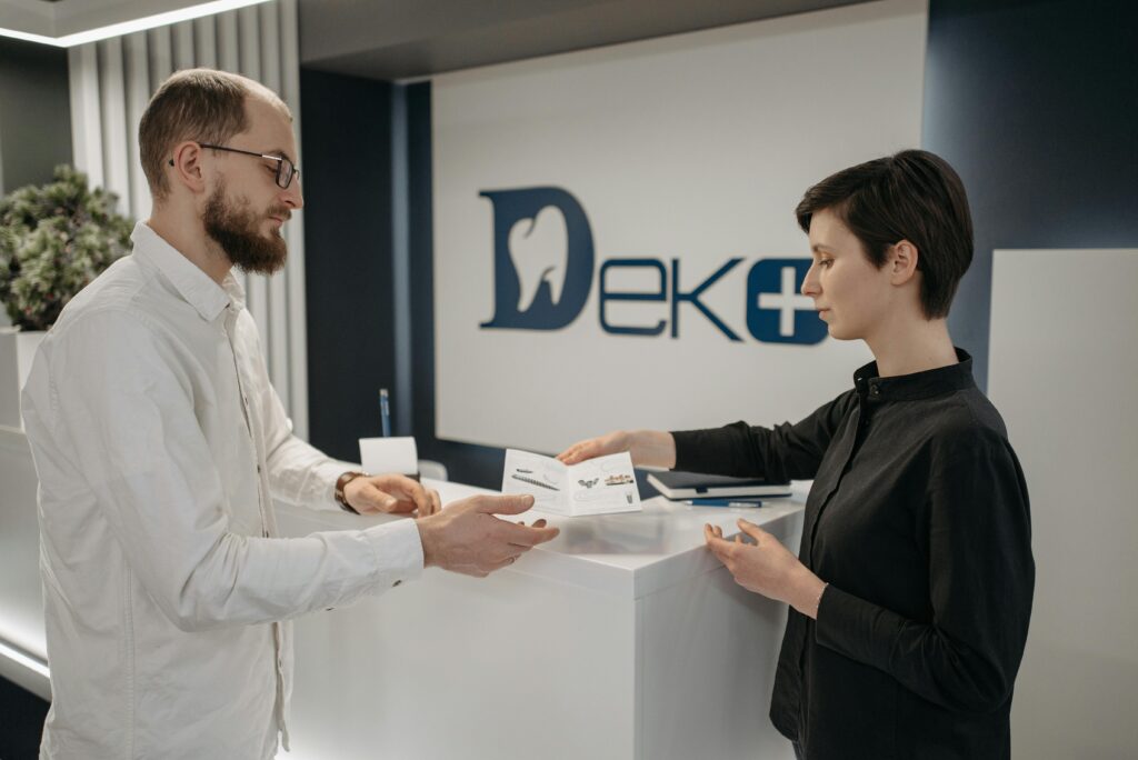 Man and woman exchanging paperwork at a modern dental clinic front desk.