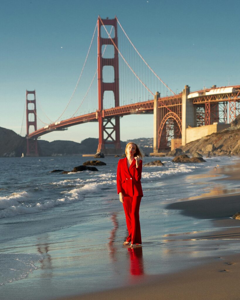 Woman in red suit on Marshall Beach with Golden Gate Bridge in background, San Francisco.