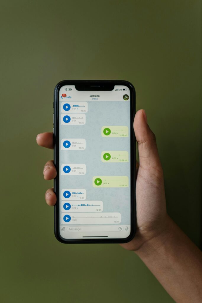 Close-up of a smartphone displaying a messaging app with voice messages in a hand.