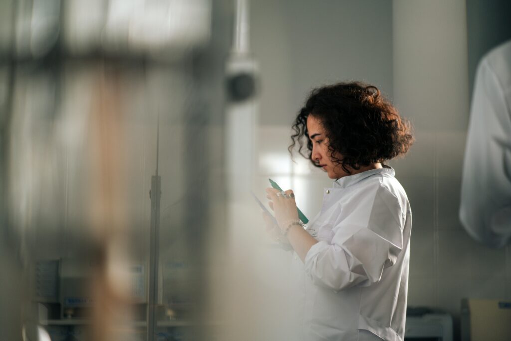 A focused female scientist with curly hair writes notes in a laboratory setting.