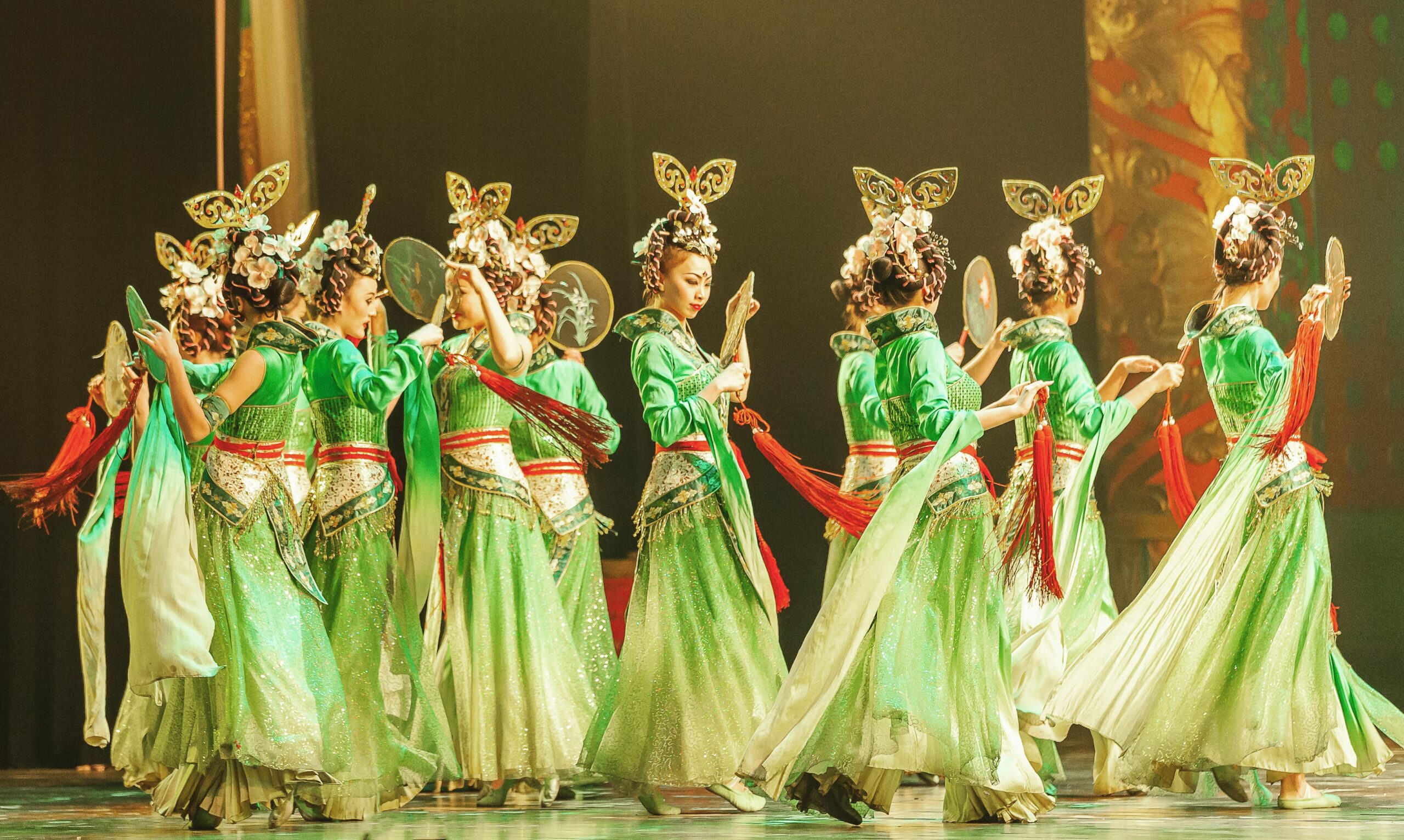 Vibrant traditional Chinese dance with women in green costumes performing on stage.