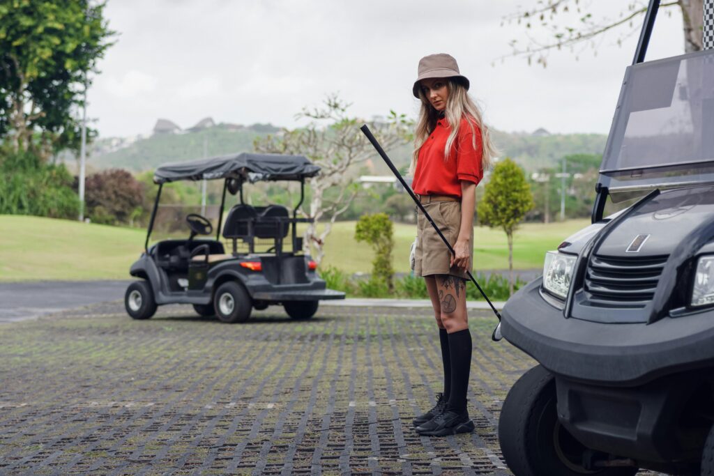 Stylish woman in a red shirt with golf cart on a vibrant golf course, embodying sporty fashion.