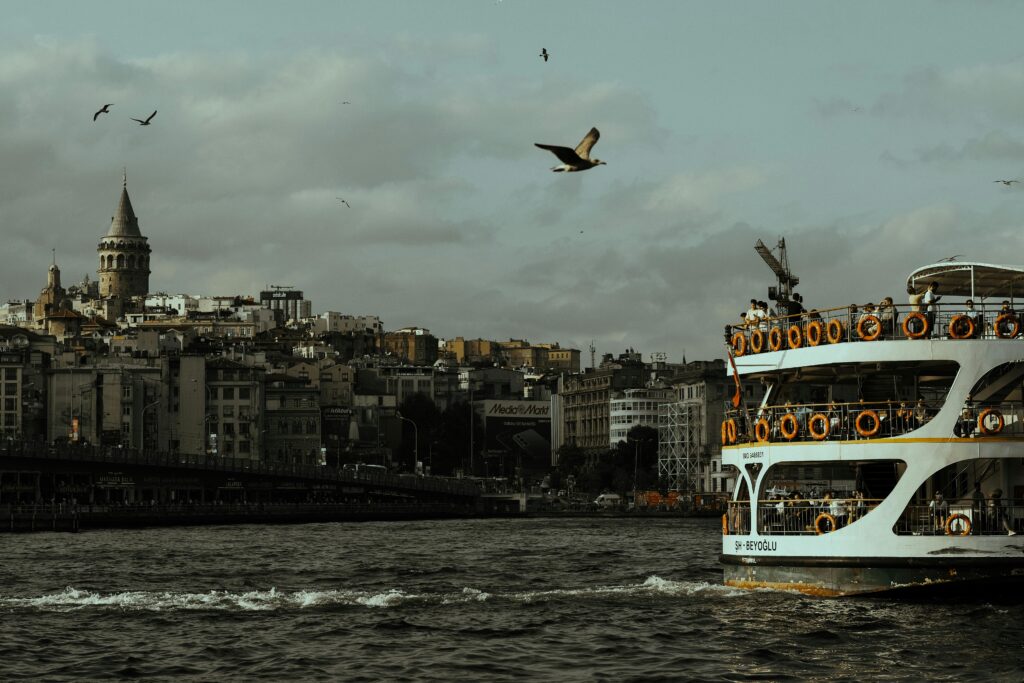 Scenic view of Istanbul's Galata Tower and a ferry on the Bosphorus shoreline, rich in urban culture.