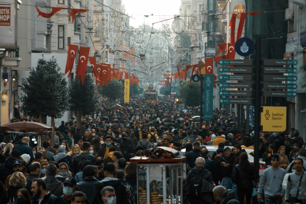 Crowded street scene in Istanbul with Turkish flags and people walking during the day.