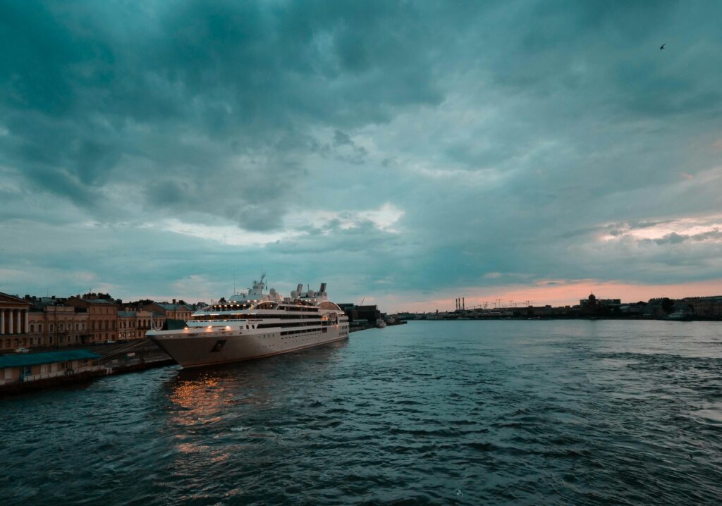 A cruise ship docked in the harbor of Saint Petersburg, Russia, under a dramatic cloudy sky at sunset.