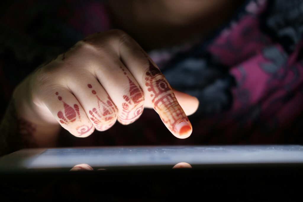 Intricate mehndi design on a woman's hand interacting with a digital tablet.