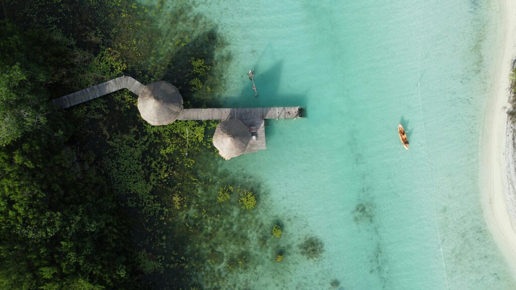 Drone shot of crystal-clear waters with jetty and boat at Bacalar Lagoon, Mexico.