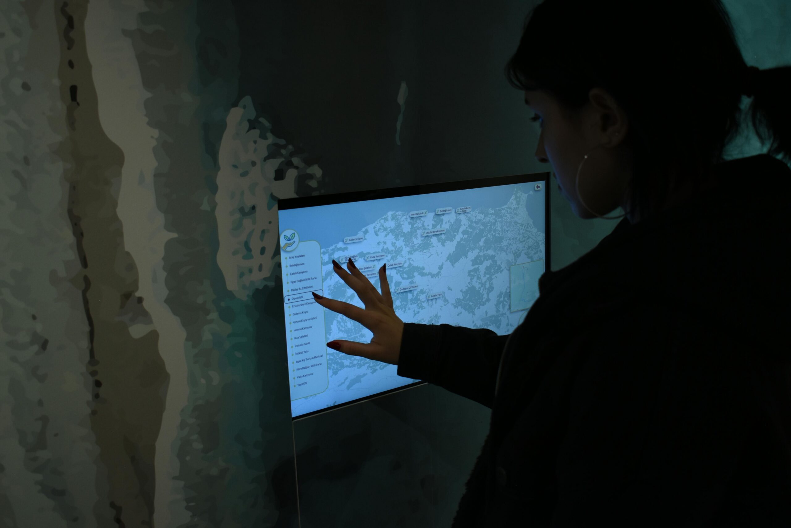 Silhouette of person interacting with a touchscreen map in a dark room.