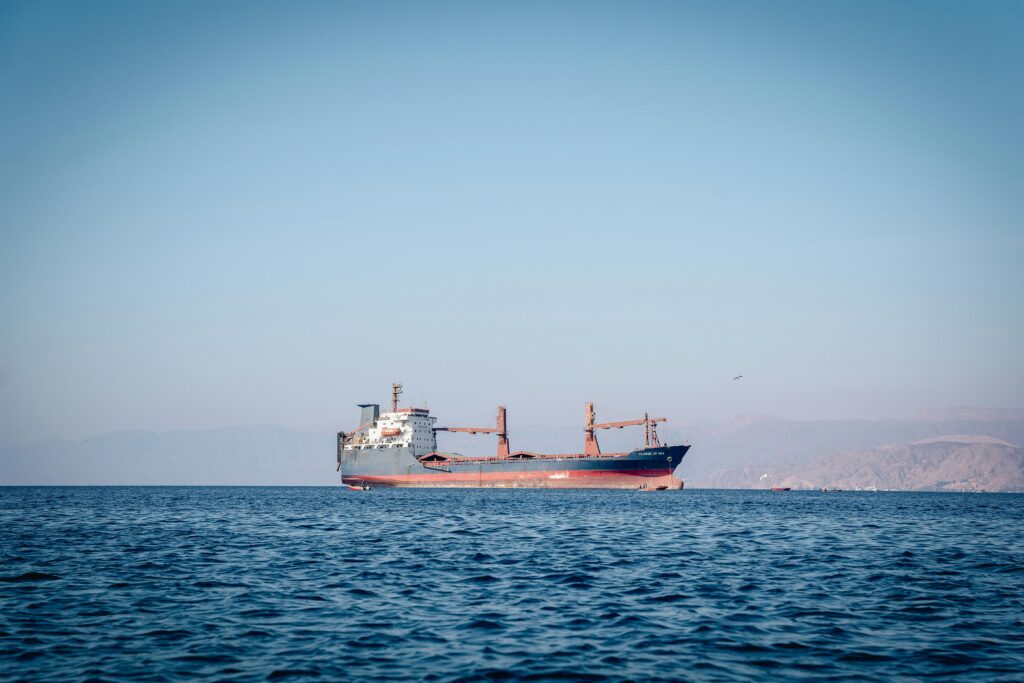 A cargo ship sailing on calm ocean waters under a clear blue sky.