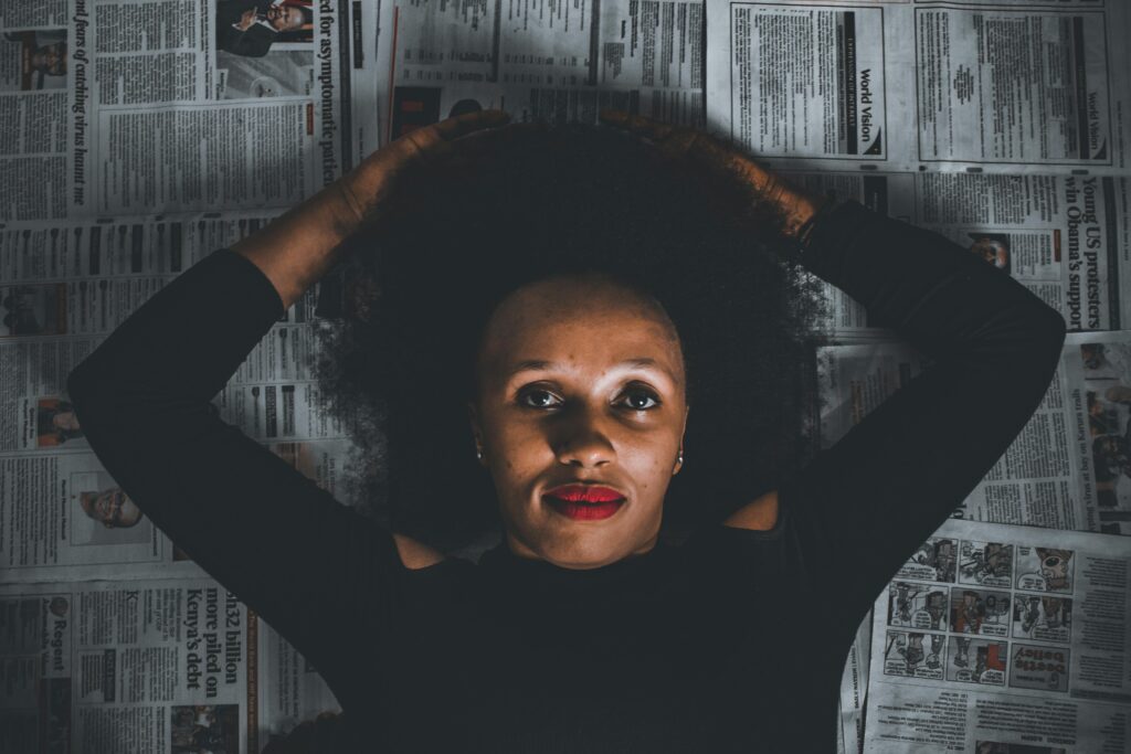 Artistic portrait of a woman with afro hair lying on newspapers, exuding confidence.