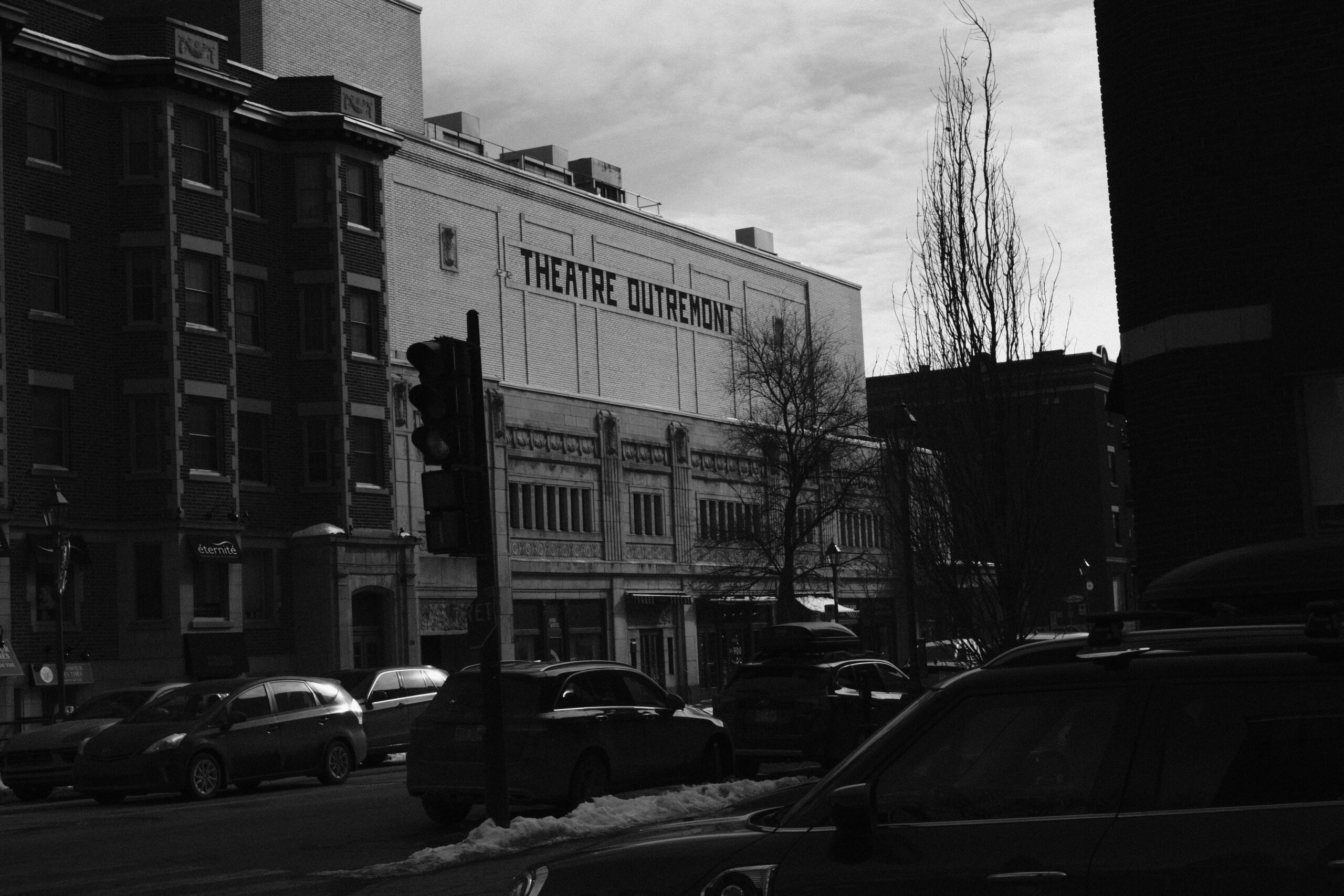 Monochrome street scene featuring Theatre Outremont in an urban setting with cars and buildings.