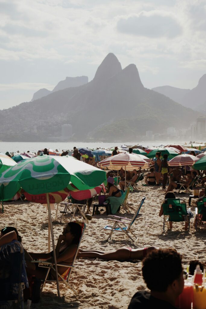 Crowded Ipanema beach with colorful umbrellas and distant mountains under a summer sky in Rio de Janeiro.