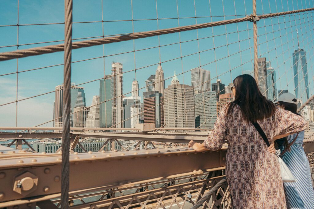 Two women enjoy the view of Manhattan skyline from Brooklyn Bridge, NYC.