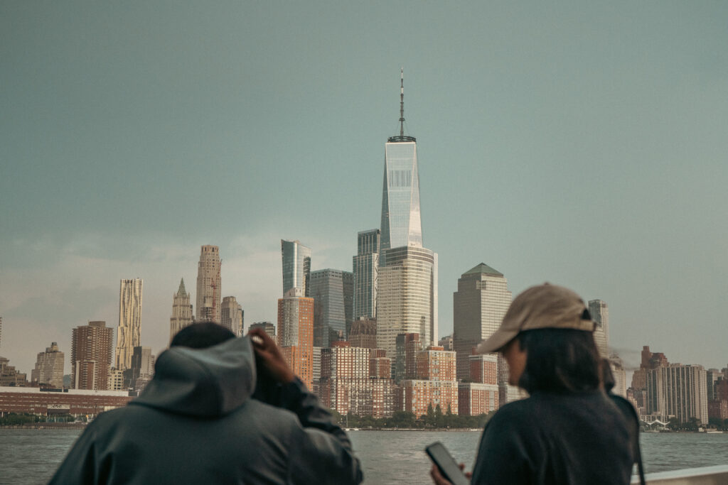 Two people admire the iconic New York City skyline with the One World Trade Center towering above.