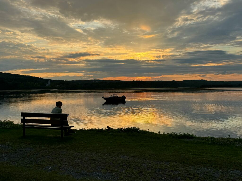Peaceful sunset view over a lake in Woodstock, NB, Canada, with a bench and boat.