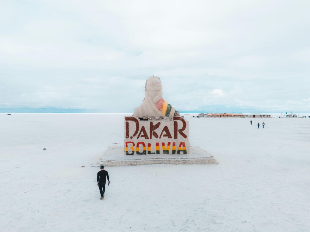 A solitary traveler approaches the Dakar Rally Monument in the vast Salar de Uyuni, Bolivia.