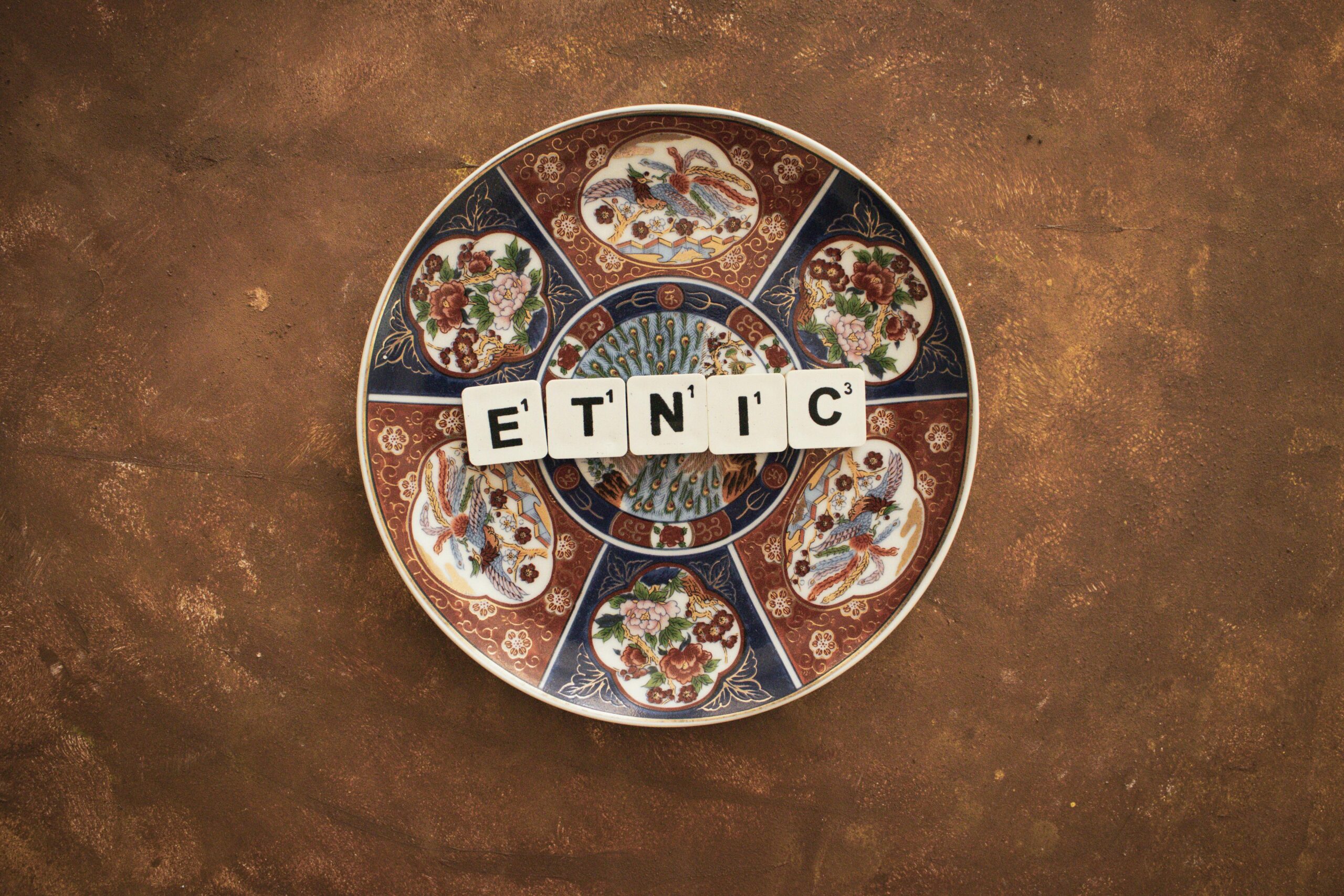 Colorful ornate plate with tiles spelling 'ETNIC' on a textured surface.