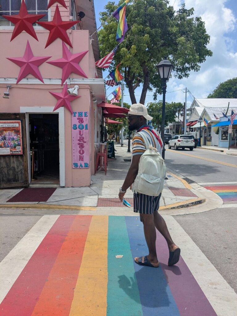 A person crossing a vibrant rainbow crosswalk in Key West, Florida, surrounded by colorful buildings.