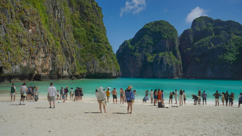 Visitors on the picturesque beach of Maya Bay in Thailand, surrounded by lush cliffs and turquoise waters.