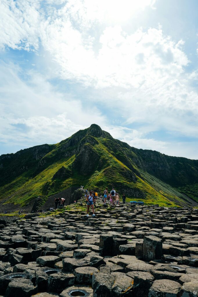 Tourists walking on the iconic basalt columns of Giant's Causeway under a bright sky.