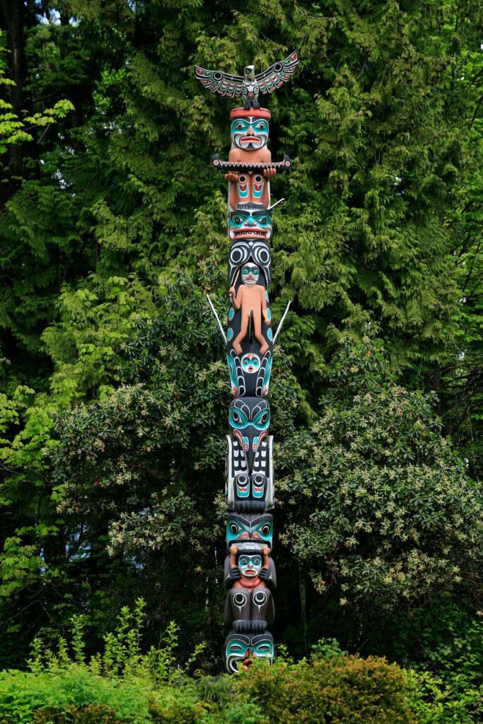 A vibrant Native American totem pole surrounded by lush green forest representing cultural heritage.