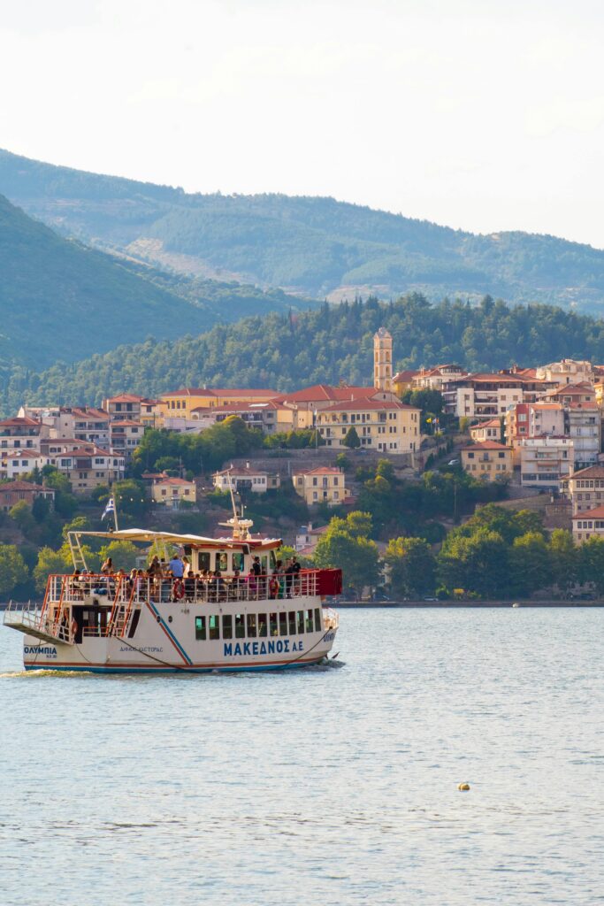 Tourist boat on Kastoria Lake with picturesque town and mountains in Greece.