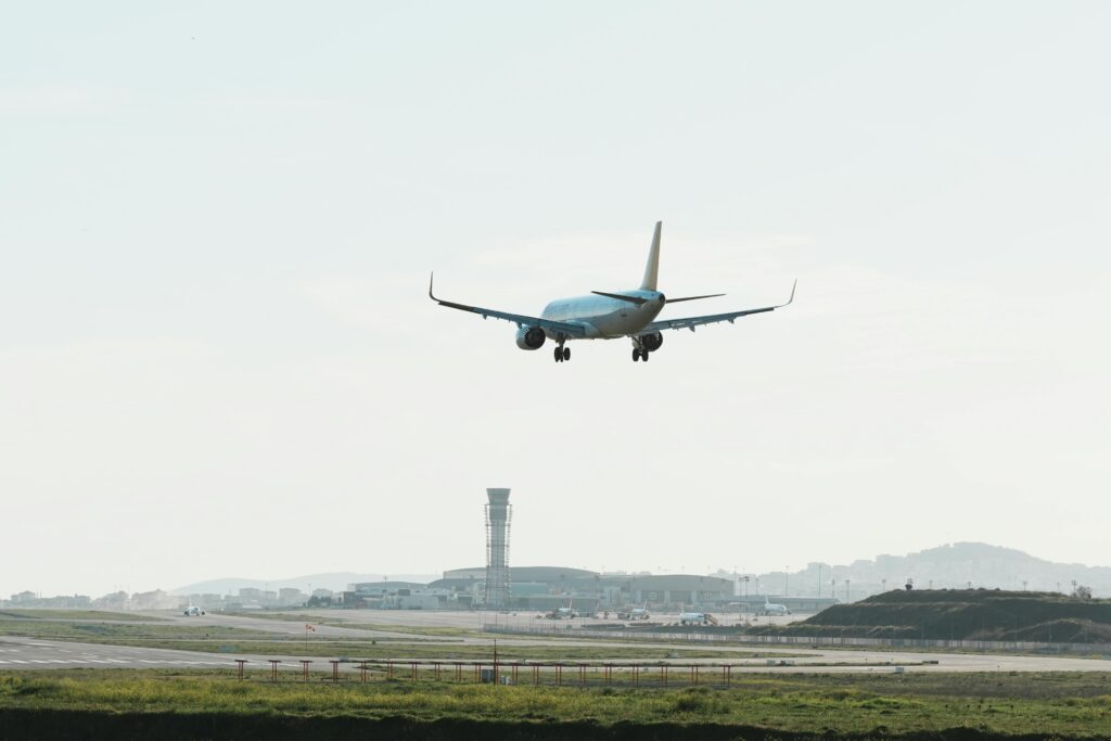 Modern airplane approaching runway for landing at a busy airport.