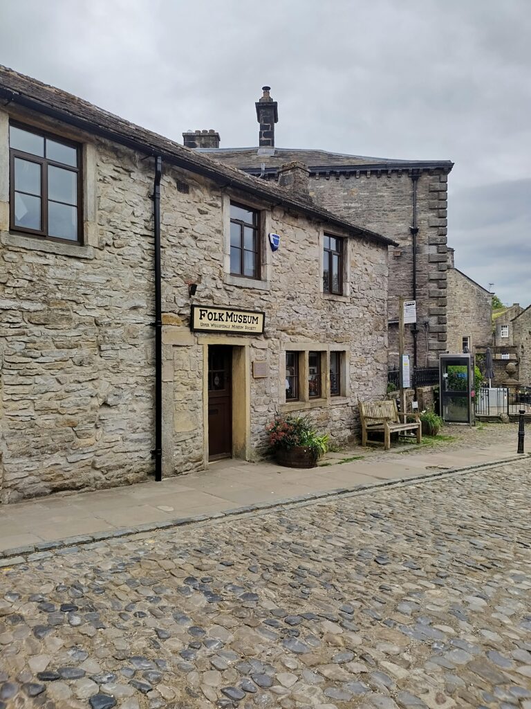 Rustic stone building housing a quaint folk museum on a cobblestone street.