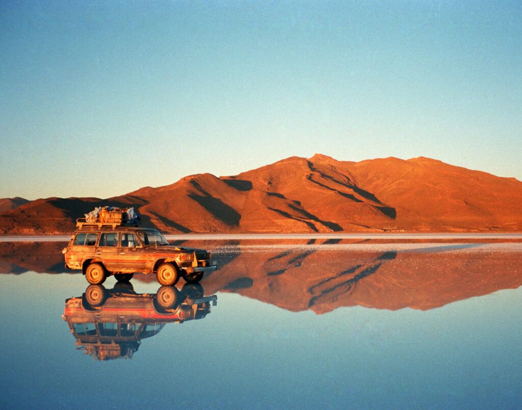 4x4 vehicle reflecting on Salar de Uyuni during sunset, Bolivia