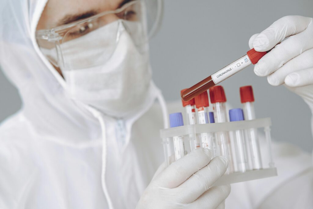 Focused young male in protective suit and gloves holding tube of blood sample with positive COVID 19 results