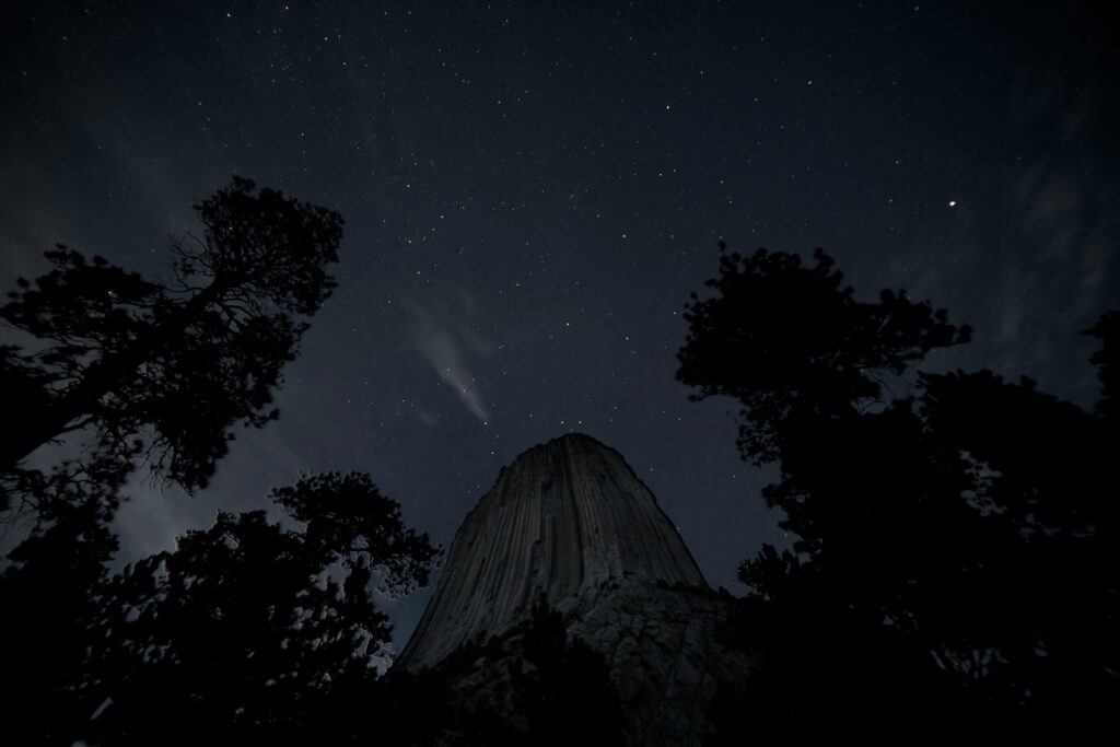 A breathtaking view of the starry sky over Devils Tower, silhouetted by trees.