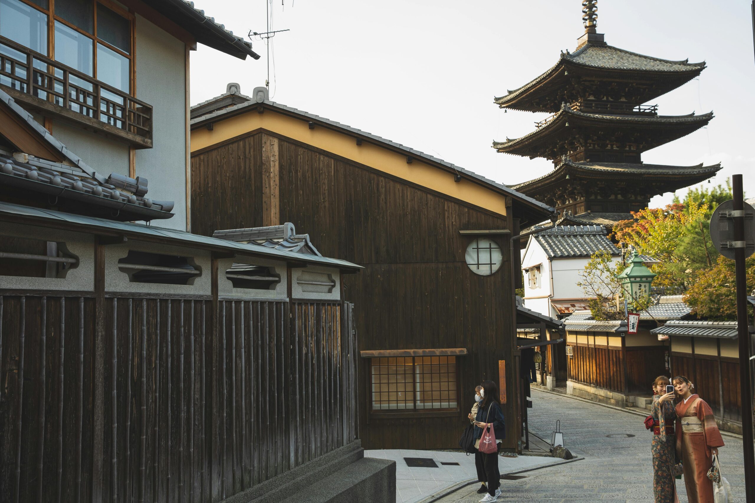 Japanese females in traditional clothes taking selfie on authentic oriental street against Asian pagoda