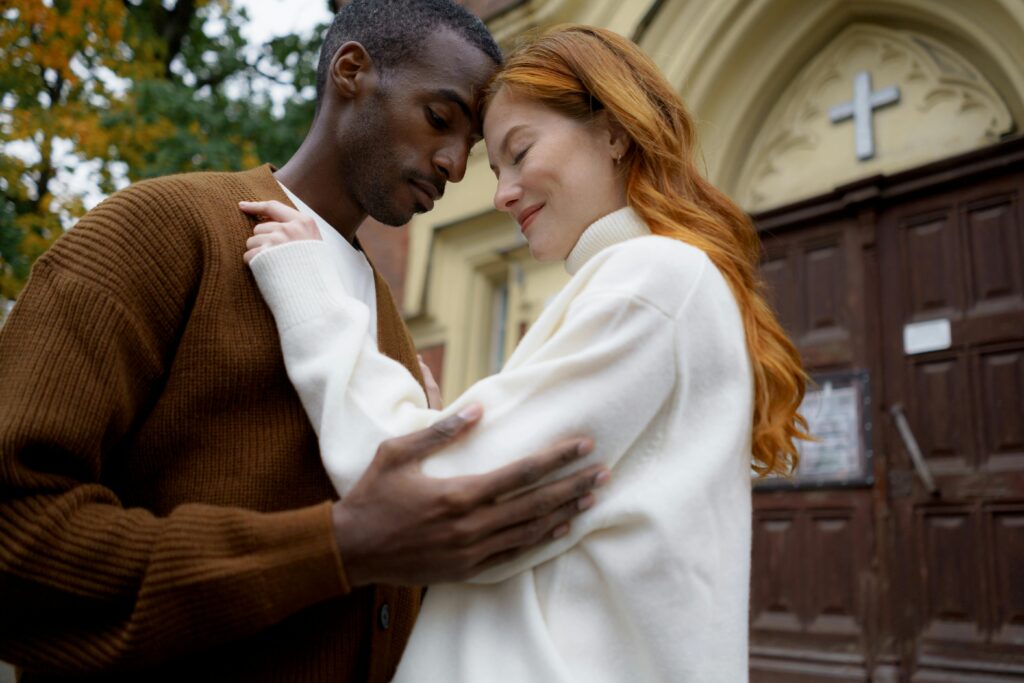 An affectionate interracial couple embraces lovingly against a classic building backdrop.