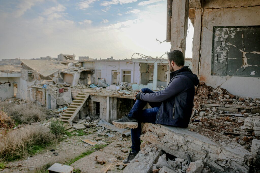 Side view of anonymous male sitting on concrete remains of broken house in desolated poor district with neglected buildings on street