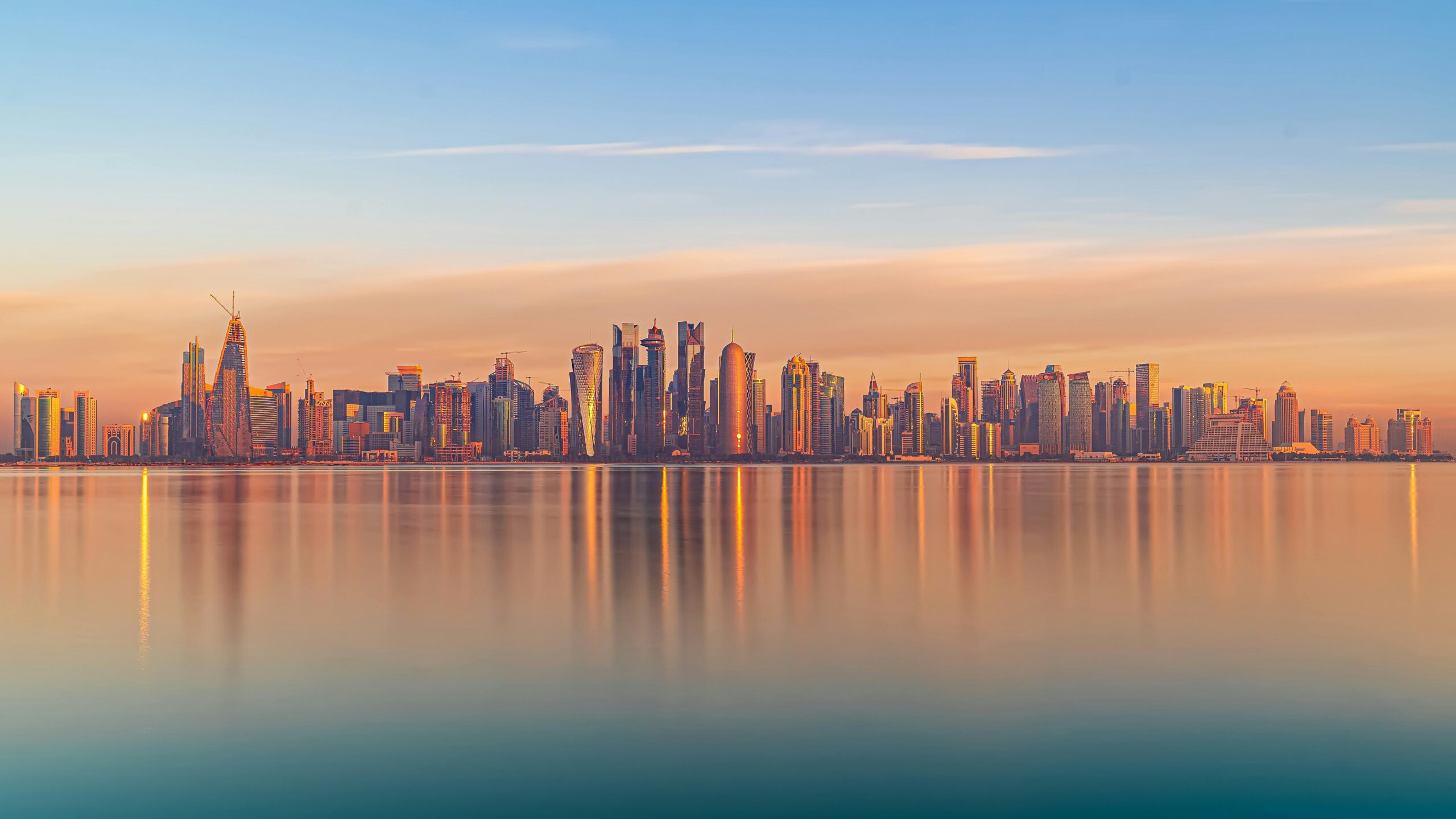 Picturesque scenery of various modern skyscrapers reflecting in calm water if sea under cloudy sunset sky in Doha