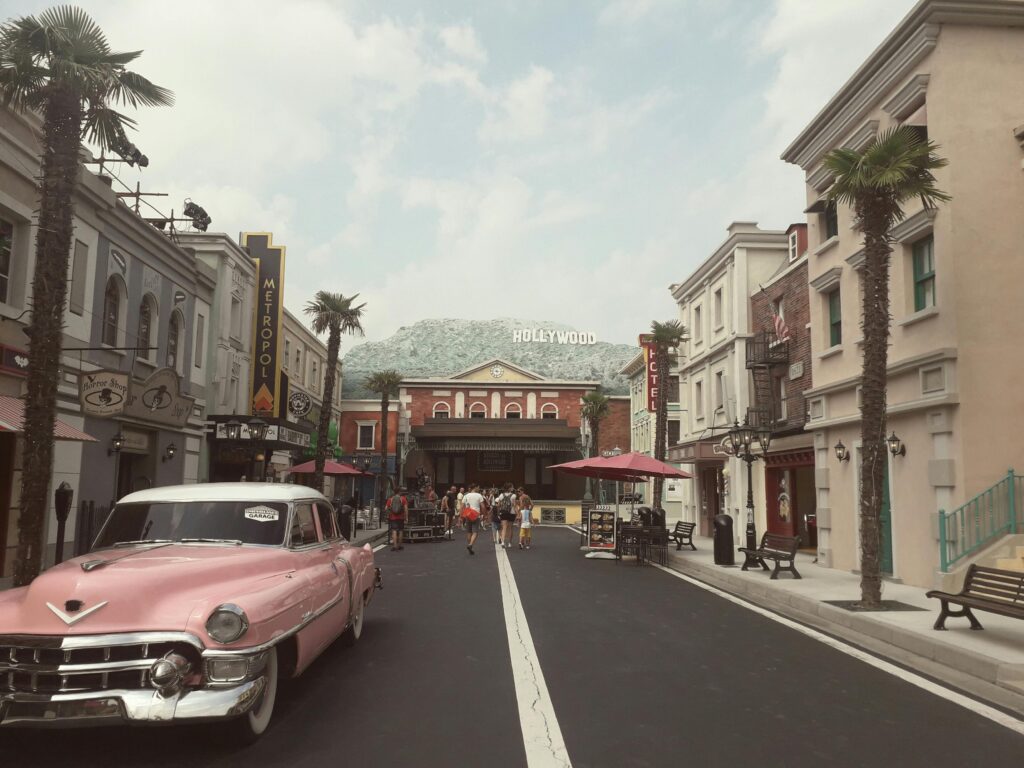 A vintage street scene featuring a pink classic car and Hollywood sign in an urban setting.