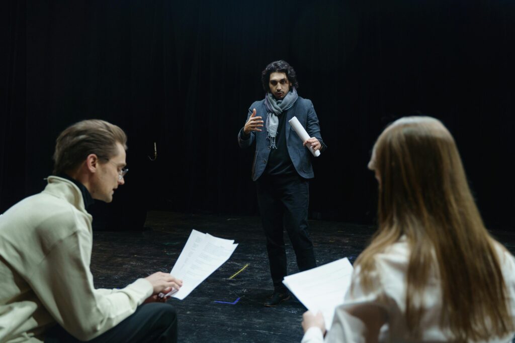 Actors and director engage in a focused rehearsal inside a theater, studying scripts intensely.