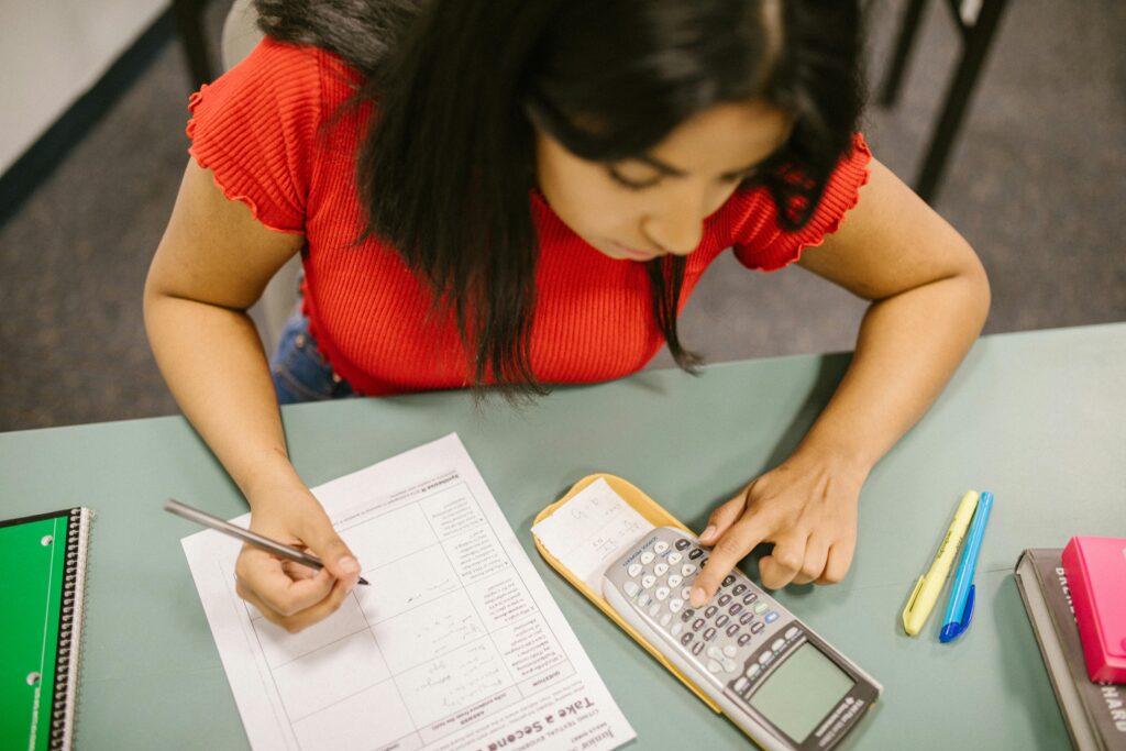 College student focusing on math test, using a calculator at a desk.